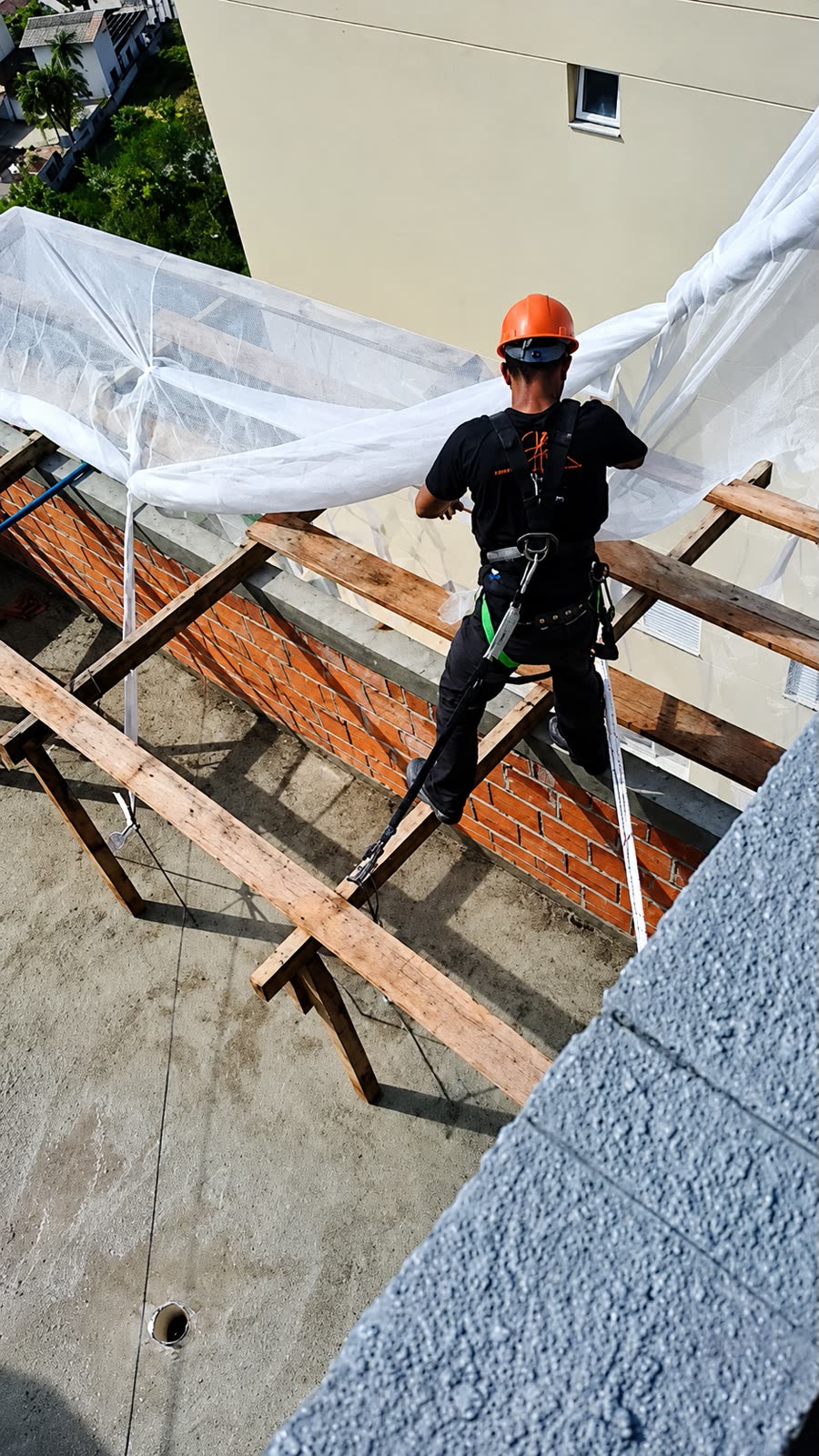 Instalador certificado com cinto de segurança e capacete montando tela fachadeira em trabalho de altura